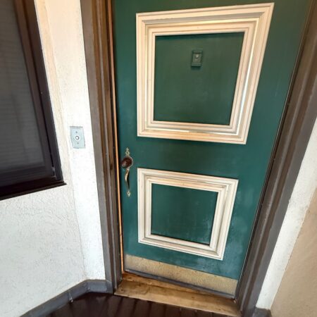 An open green front door with a freshly drilled hole prepped for a new lock installation.