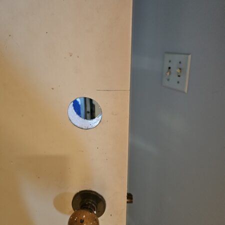 A clean hole drilled into a white interior door above a brass doorknob for a new lock.