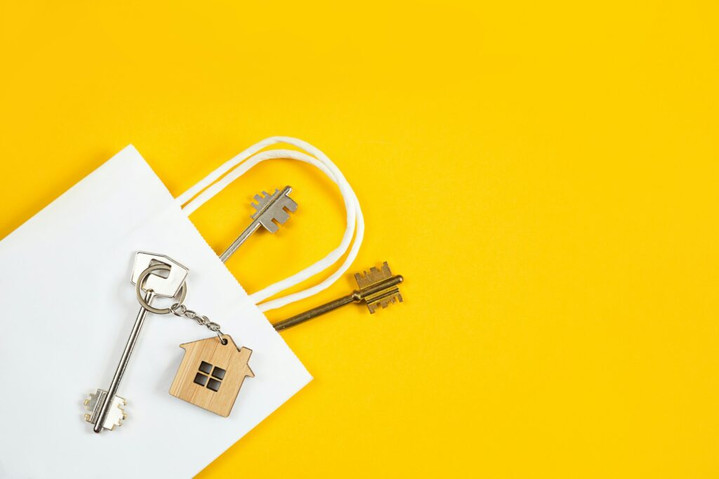 Key ring in the shape of wooden house with key on a yellow background in a white paper gift wrapping