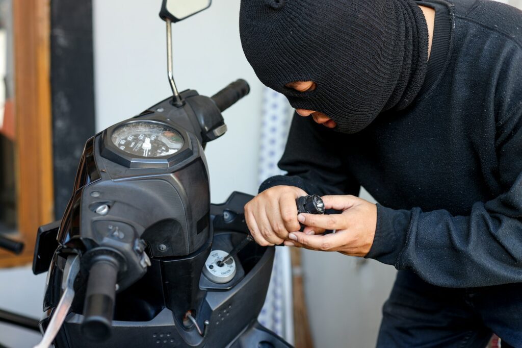 Motorcycle thief in black mask trying to unlock the ignition key of motorcycle with screwdriver.
